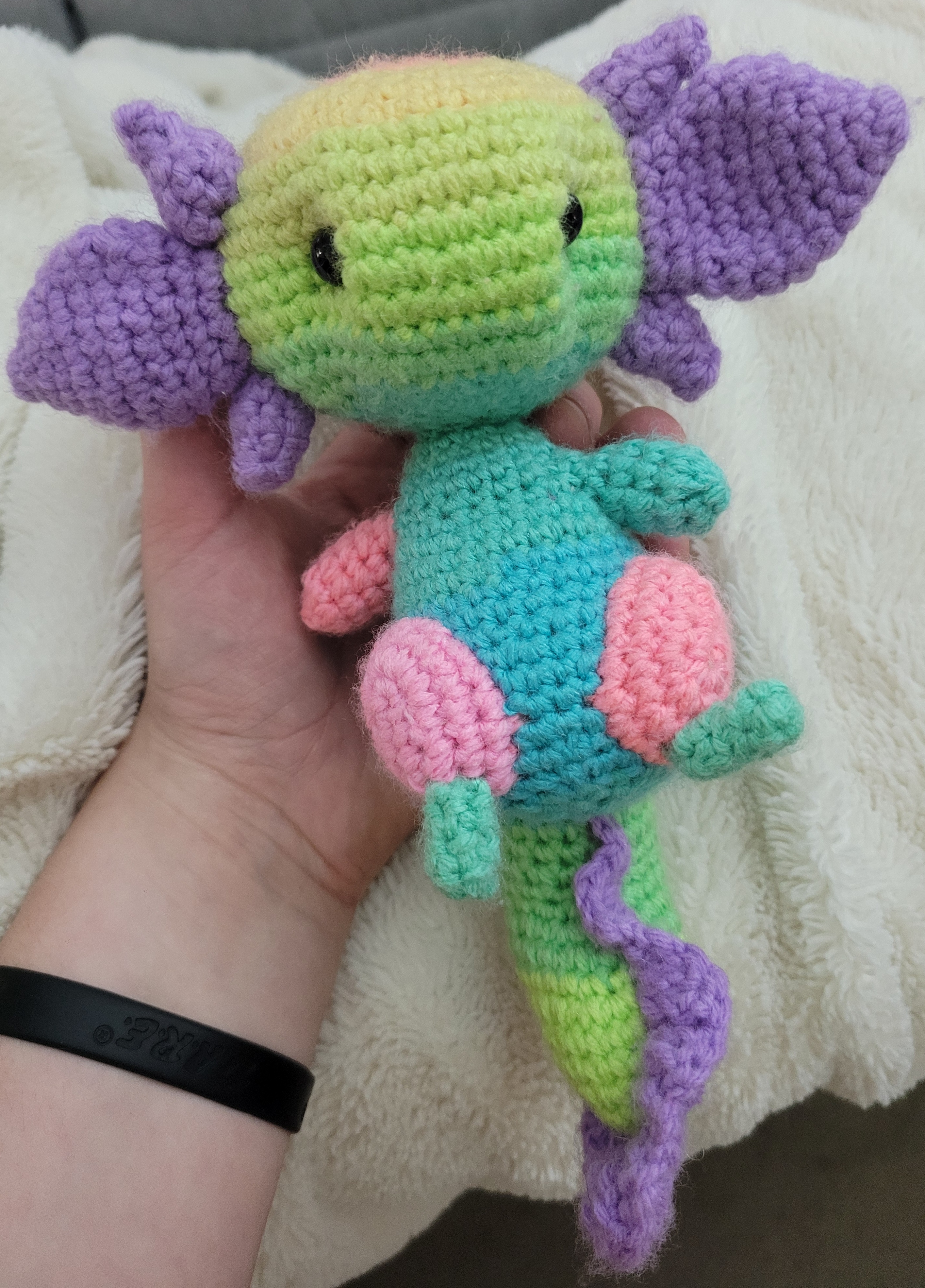 Pastel crochet axolotl with a green head, purple gills, turquoise body, and pink feet.